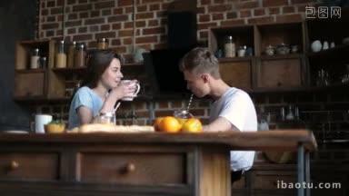 相爱的年轻夫妇在家庭厨房共度美好的早晨英俊的潮人喝着玻璃瓶里的橙汁